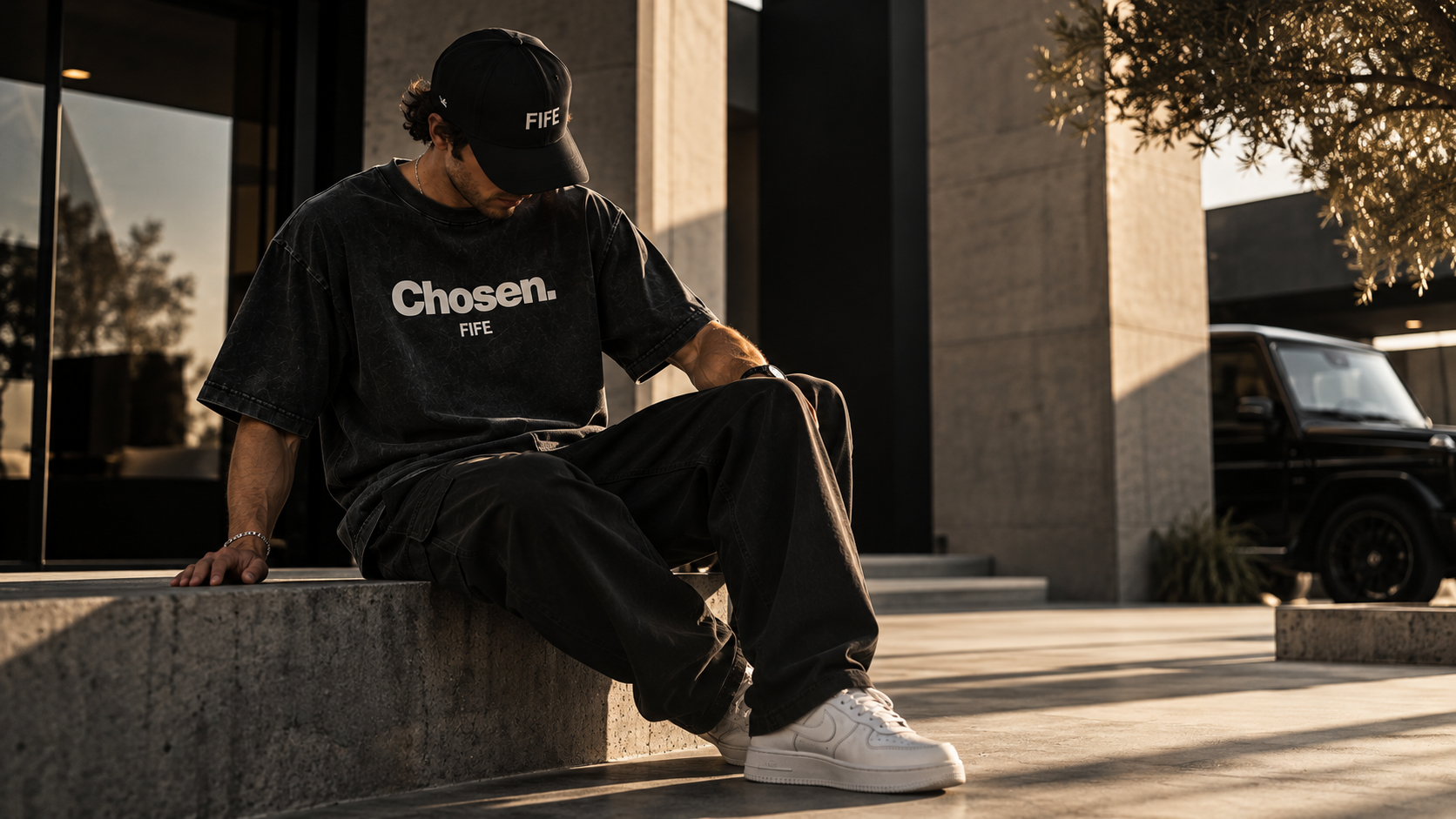 Man in a black FIFE Chosen. tee and FIFE cap seated in golden light